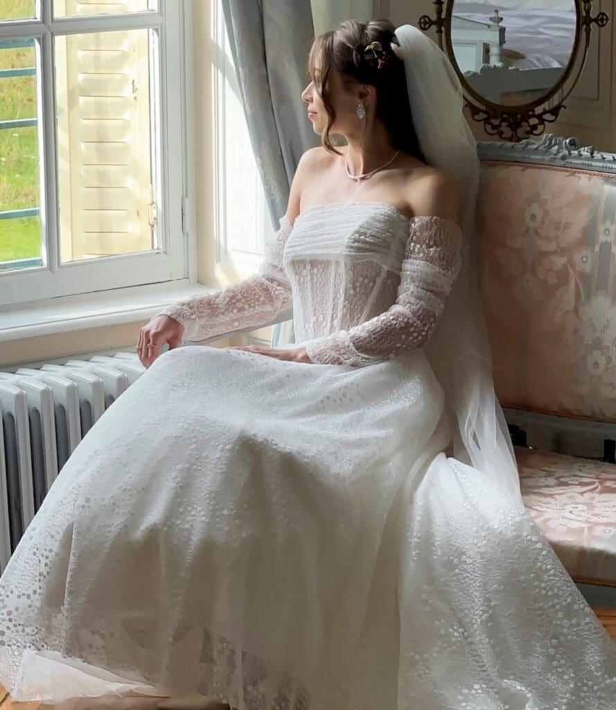 Bride with elegant hair and natural makeup looking out the window of the Blue Suite at Château de Bonnemare in Normandy